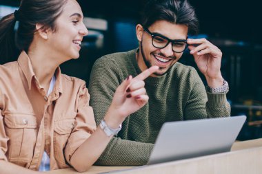 Neşeli ve erkek öğrencilerin ödev birlikte, gülümseyen hippi kız erkek komik şakalara gülüyor konuşurken bir şey üzerinde işaret yapmayı işbirliği olumlu konuşmayı