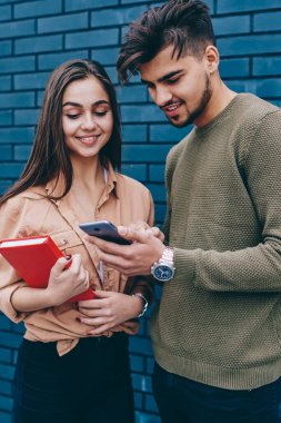 Erkek ve dişi hipsters akıllı telefonlar, onun kız arkadaşı birlikte ücretsiz vakit cep telefonunuzda fotoğraf ve video gösterilen olumlu hipster adam için yeni modern uygulaması hakkında konuşmayı gülümseyen