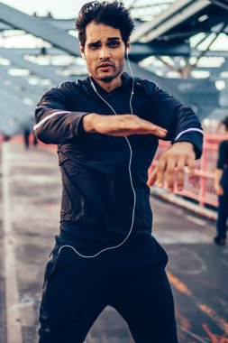 Kardiyo egzersiz ile şehir Köprüsü, eğitim açık havada sırasında gayreti ve kameraya bakarak kas hipster adam kulaklıktan dinleme ses kaseti süre yapıyor spor genç sağlıklı adam