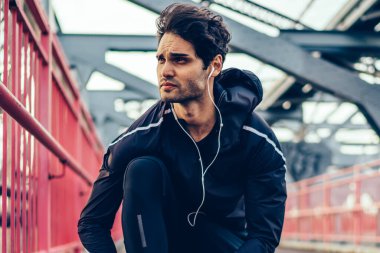 Runner adam uygulamakla Spor Ayakkabı bağcıklarımı köprüde dinleme ses kayıtları sırasında elektronik kulaklık Avrupa jogger spor eşofman açık havada kardiyo egzersizleri için hazırlık içinde çalıştırmak hazırlanıyor