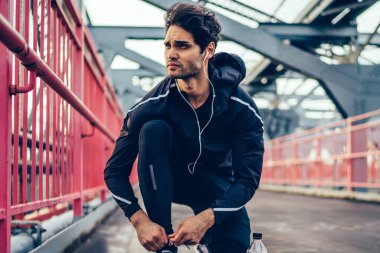 Runner adam uygulamakla Spor Ayakkabı bağcıklarımı köprüde dinleme ses kayıtları sırasında elektronik kulaklık Avrupa jogger spor eşofman açık havada kardiyo egzersizleri için hazırlık içinde çalıştırmak hazırlanıyor