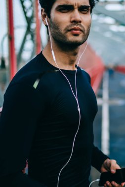 Smartphone aygıtı elinde tutan ve açık havada, başlangıç koşu önce kameraya bakarak ciddi erkek koşucu spor egzersiz sonrası kas vücut kulaklık ile müzik dinleme adamla konsantre