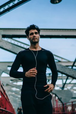 Radyo smartphone medya uygulaması, açık havada koşu sırasında genç sporcu eğitim vücut kullanarak elektronik kulaklık ile müzik keyfi sırasında şehir Köprüsü üzerinde çalışan gücü Erkek atlet