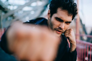 Erkek bulanık cephe süsleme, ciddi Avrupa sporcu mücadele spor kameraya seyir sırasında kentsel ayarı uygulamak ve güç yumruk yaparak eşofman içinde yarım uzunluk portre yumruk sıkılı