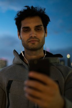 Etkin atletik sporcu kardiyo tatilinde mobil uygulama aracılığıyla metin mesajları okuma, açık havada, telefonda sohbet ve akşam koşu sonra müzik keyfi Avrupa erkek koşucu egzersizleri