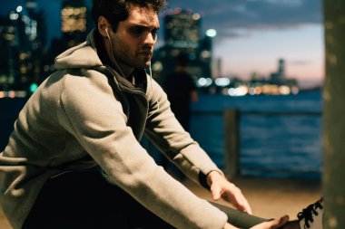 Avrupa erkek koşucu duygu acı sonu duvarının yakınında akşam egzersiz yaparken müzik çalma dinlerken Başlarken iyi, sporcu için esneklik egzersizleri yapıyor gece şehir genelinde çalıştırdıktan sonra bacak üzerinde