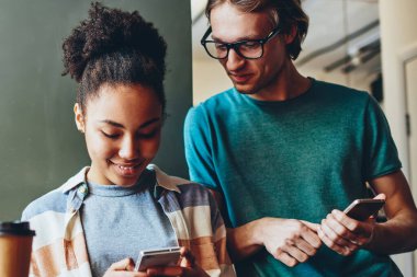 Olumlu çok ırklı arkadaşlar, akıllı telefon bluetooth bağlantısıyla cep telefonundan video izleyip sohbet eden neşeli erkek ve kız öğrenciler üzerinden multimedya dosyalarını paylaşıyorlar.