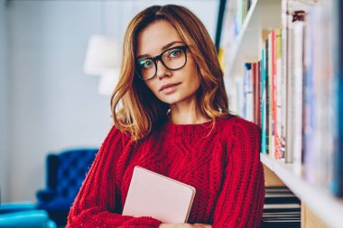 Gözlük eğitim için ders kitabı tutarak ve kameraya, Genç beyaz büyüleyici kadın kitapçı zaman harcama seyir vizyon düzeltme için çekici hippi kız portresi yarım uzunluk