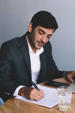 Genç Hintli işadamı masaüstü dizüstü bilgisayar aygıt ve su, yakışıklı işveren netbook hakkında bilgi aramak için vakit oturan ders kitabı zevk kağıt iş planı yazma