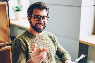 Neşeli hipster erkekte olumlu erkek konuşuyor ve klasör elinde tutan gülümseyerek trendy gözlük rahat ofisinde çalışması sırasında meslektaşı ile heyecan görüşme yapma fotoğraf kırpılmış