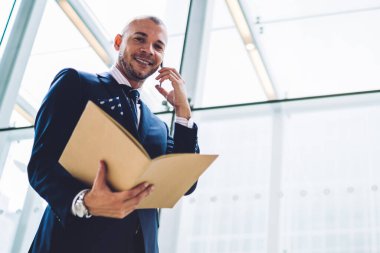 Başarılı bir iş adamı portresi altında klasör belgeler ile smartphone aygıtında çağrılırken tutan formal giyim giymiş. Ofis Binası telefonda konuşurken müreffeh gurur ceo
