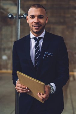 Klasör el kameraya gülümseyen Ise tutarak pahalı şık elbiseli başarılı olumlu işadamı portresi. Formal giyim daimi cam duvara neşeli Finans Müdürü