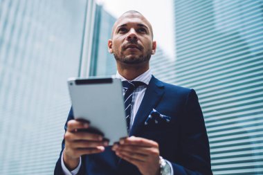 Şık resmi genç gurur CEO'su görünümünün altındaki dijital dokunmatik yüzey elinde tutan ve yüksek gökdelenler ile modern şehir merkezinin kentsel ortamda ayakta modern ofis arama giymek