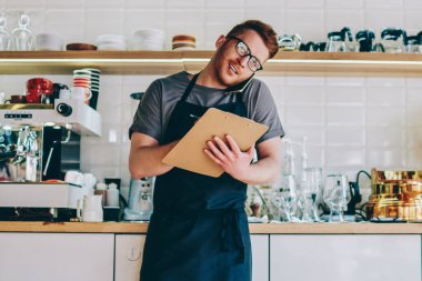 Siyah önlük kafede beyaz erkek sahibi ayakta karşı bar-makine ve smartphone ürün sipariş için geliştirme iş yapmak için aradım. Cep üzerinde konuşurken Restoran çalışanı