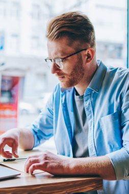 Bilgi okuma ve kahve dükkanında kablosuz Internet bağlantısı kullanarak modern bilgisayarda çalışan veri kontrolü hipster öğrenci konsantre. Dalgın genç adam netbook sınav hazırlama