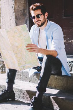 İlginç yerleri olan mutlu stil sahibi genç adam harita okuyor ve şehrin aşağısındaki mimari merdivenlerde otururken rotasını belirliyor. Olumlu sakallı turistler tatil beldelerini arıyor.