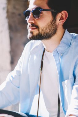 Siyah güneş gözlüğü takan sakallı turistin kırpılmış görüntüsü. Havalı günlük giysiler giymiş düşünceli bir gezgin. Elinde harita var.