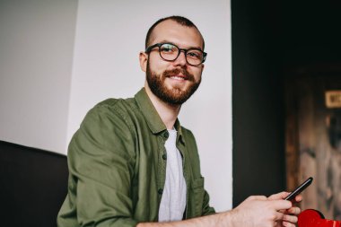 Yakışıklı hipster adam laptop, cep telefonu için sohbet ve paylaşım smartphone multimedya dosyaları ile netbook için bluetooth bağlantısı kullanarak tutan serbest meslek işten dikkati portresi