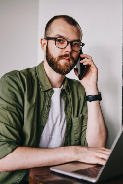 Hipster gözlük cep telefonu en iyi arkadaşı ile iletişim içinde zeki öğrenci yeni modern elektronik aygıtlar kullanarak okuyan için üniversite kafeterya, 20 yaşında adam otururken portresi