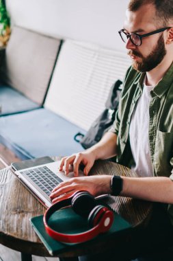 Çatı katı iç ve uzaktan çalışma ile kafede oturan gözlük ciddi yetenekli beyaz programcı, genç düşünceli laptop ve fikirler için kurs metin yazarak izlerken webinar adam.