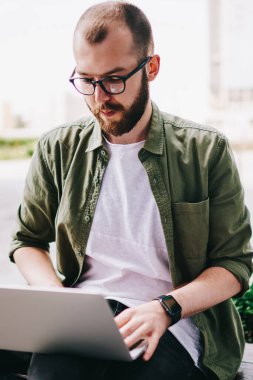 Dizüstü bilgisayar ile bankta oturmuş ve yeni modern elektronik aygıt için Gözat Web sitesi kullanarak proje hazırlama webinar online, profesyonel programcı izlerken kendinden emin ve düşünceli genç adam