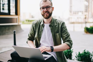 Dizüstü bilgisayarda çalışarak ve açık havada, oturan kameraya kampüsünde öğrenme netbook üzerinde bilgi arama hipster adam arıyor gözlük içinde gülümseyen genç profesyonel serbest meslek portresi