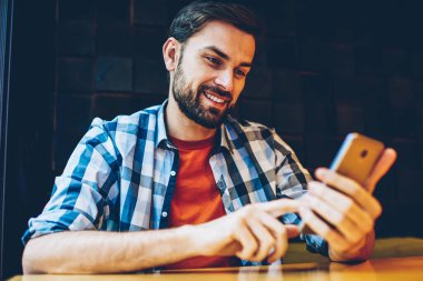 Neşeli sakallı genç adam komik Haberler Blog için 4 g bağlı smartphone aygıt üzerinde okuma rahat kıyafet giymiş Internet. Pozitif hipster adam modern cep telefonu online video izliyor