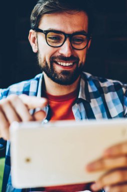 Modern tablet tarihinde yayına izlerken gözlük olumlu sakallı hippi adam bağlı 4 g için Internet. Casual kıyafet online dijital dokunmatik ped cihaz üzerinde sohbet içinde neşeli erkek blogger