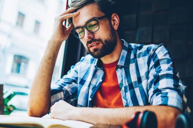 Dalgın akıllı edebiyat kitap okuma ve yaklaşan sınavlar için hazırlık öğrencisi sakallı. Akıllı genç adam eğitim görev Üniversitesi'nde ders kitabı ile masada oturan çözme üzerinde düşünme konsantre