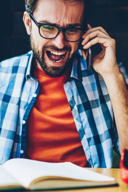 Öfkeli sakallı hippi dijital Smartphone cep telefonu ile telefon görüşmesi sırasında bağıran adam. Kızgın genç adam savunarak ve modern hücresel aygıt vasıl okul sırası ders kitabı oturan: çağrı anlaşmazlık çözme