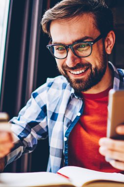 Smartphone cep telefonu ile internet bağlantısı ile internet sitesinde ödeme yapmadan elinde banka kartı ile neşeli sakallı öğrenci. Kartvizit para hareket için telefon tutarak bakarak olumlu genç adam