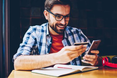 Mutlu erkek blogger banka kartı elinde tutan ve yüksek yolu ile online ödeme yapmak için akıllı telefon numarasını çevirirken 20 yaşında hızda internet. Hücresel harekette yapan başarılı genç erkek