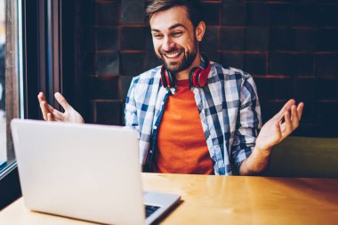 Mutlu sakallı hippi blogger modern dizüstü bilgisayarda görüntülü görüşme yoluyla arkadaşlarınızla iletişim kurmak için kablosuz 4 g bağlı internet. Komik eğitsel bir netbook izlerken boyun kulaklık ile pozitif genç adam