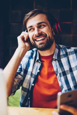 Telefon için Bluetooth kulaklık elektronik müzik zevk olumlu sakallı blogger bağlı. Neşeli rahat giyinmiş genç adam dinleme ses şarkı çalma listesinden Smartphone'da indirilen