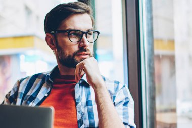 Düşünceli sakallı grafik tasarımcı düşünme üzerinde Web sitesi geliştirme ve modern dizüstü cihaz alan coworking içinde ücretsiz 4 g internet bağlantısı kullanarak, serbest çalışma pencereden dışarı seyir için fikirler