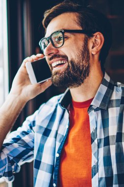 Mutlu sakallı hippi adam gözlük sırasında telefon konuşma bir arkadaşım Smartphone cep telefonu ile gülüyor. Gülümseyen ve dijital cep telefonu üzerinde konuşurken rahat şık gömlek giymiş olumlu genç adam