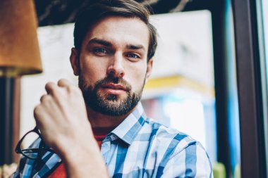 Yarım uzunluk portre yakışıklı genç adam gözlük kahvehane iç dinlenme elinde tutarken kameraya bakan sakallı. Şık gömlek kafede oturan adam iyi görünümlü hipster