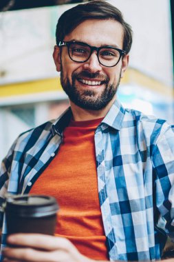 Yarım uzunluk portre gitmek başarılı sakallı genç adamın gözlük kamera ile kahve oturan gülümseyen vizyon düzeltme için coworking içinde eller. Pozitif hipster adam rahat gömlek giymiş