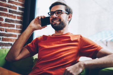 Sakallı smartphone aygıt üzerinde arama olumlu hipster adam arkadaşıyla görüşme ayarlamak için. Şık gözlük modern cep telefonu kafede oturan iç konuşurken neşeli genç adam