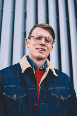 Neşeli genç öğrencinin yarım uzunluk portre kameraya gülme şık denim giyim giymiş. Kentsel ortamda poz vizyon düzeltme optik gözlük olumlu hipster adam