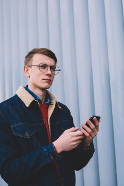 Düşünceli şık giyimli erkek blogger yayın 4 g internet bağlantısı açık havada kopyalama alanı alanı ile duvarının yakınında yürüyüş yolu ile Smartphone cep telefonu ile sosyal ağlar medya paylaşımı sırasında üzerinde durulması