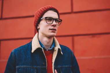 Kırmızı şapka ve şık optik gözlük planları kentsel ortamda yürüyüş sırasında düşünme düşünceli genç yakışıklı adam. Düşünceli hipster adam fikir ayakta yakınındaki promosyon arka plan üzerinde durulması