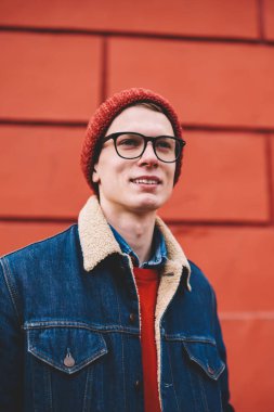 Vizyon Düzeltme açık havada kırmızı promosyon arka plan üzerinde duran için optik gözlük rüya gibi neşeli hipster adam. Giyinmiş olumlu genç adam uzakta şık casual kıyafet arıyorum