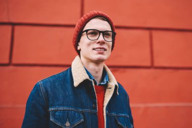 Vizyon Düzeltme açık havada kırmızı promosyon arka plan üzerinde duran için optik gözlük rüya gibi neşeli hipster adam. Giyinmiş olumlu genç adam uzakta şık casual kıyafet arıyorum