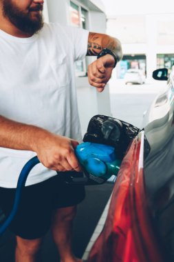 Hipster bir adamın benzin istasyonunda arabasına benzin koyarken kol saatine baktığı görüntüler. Delikanlı, benzin deposu hortumla yakıt ikmal aracını kontrol ederken zamanı kontrol ediyor.