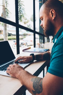 Ciddi genç adam netbook daktilo metni hakkında bilgi arıyor, yetenekli erkek klavye dizüstü bilgisayarda ve kafeteryada internet bağlantısı üzerinden internet sayfalarını tarıyor