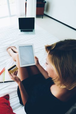 Yatağın üzerinde otururken kredi kartı numarasını kullanan genç hippi kız, taşınabilir bilgisayarla online alışveriş yapıyor rahat bir evde boş zaman geçiriyor.