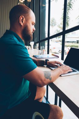 Kafeteryadaki masada oturan ciddi bir erkek serbest yazar ağ kurmak ve sohbet etmek için dizüstü bilgisayarı kablosuz internete bağlıyor. Düşünceli hispter adam internet sayfasında bilgi araştırması yapıyor.