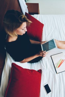 Sosyal medyadan gelen bilgileri okuyan kadın blogcu portatif bilgisayarı yatakta tutarken, genç kadın serbest çalışan ev içi rahatlığında dijital tablet kullanarak e-postalarını kontrol ediyor.