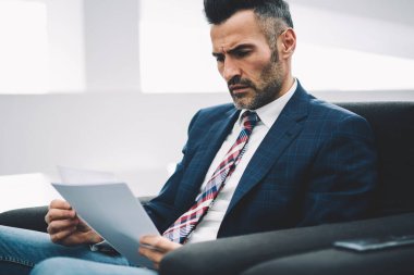 Konsantre deneyimli olgun gurur CEO'su muhasebe raporları, office koltukta oturan kağıtlara okuma formal giyim giymiş. Dalgın işadamı 50 yaşında mali bilgilerini kontrol